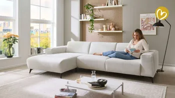 Frau sitzt gemütlich auf einem Sofa und ließt ein Möbelmagazin